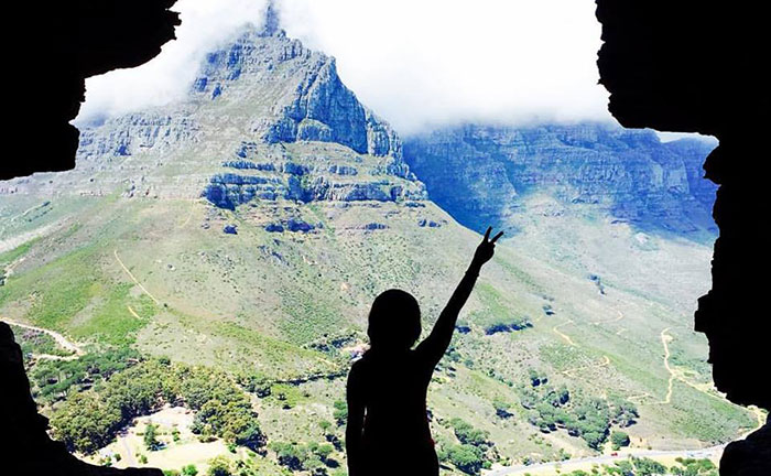 A student stands at the opening of a cave overlooking a vast canyon that leads back up into a misty mountain